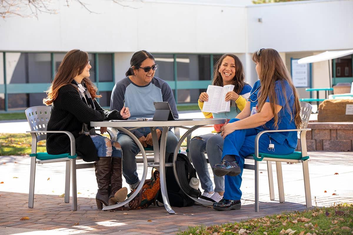 Four 太阳集团娱乐场登陆网站 students sitting at a table outside conversing and smiling.